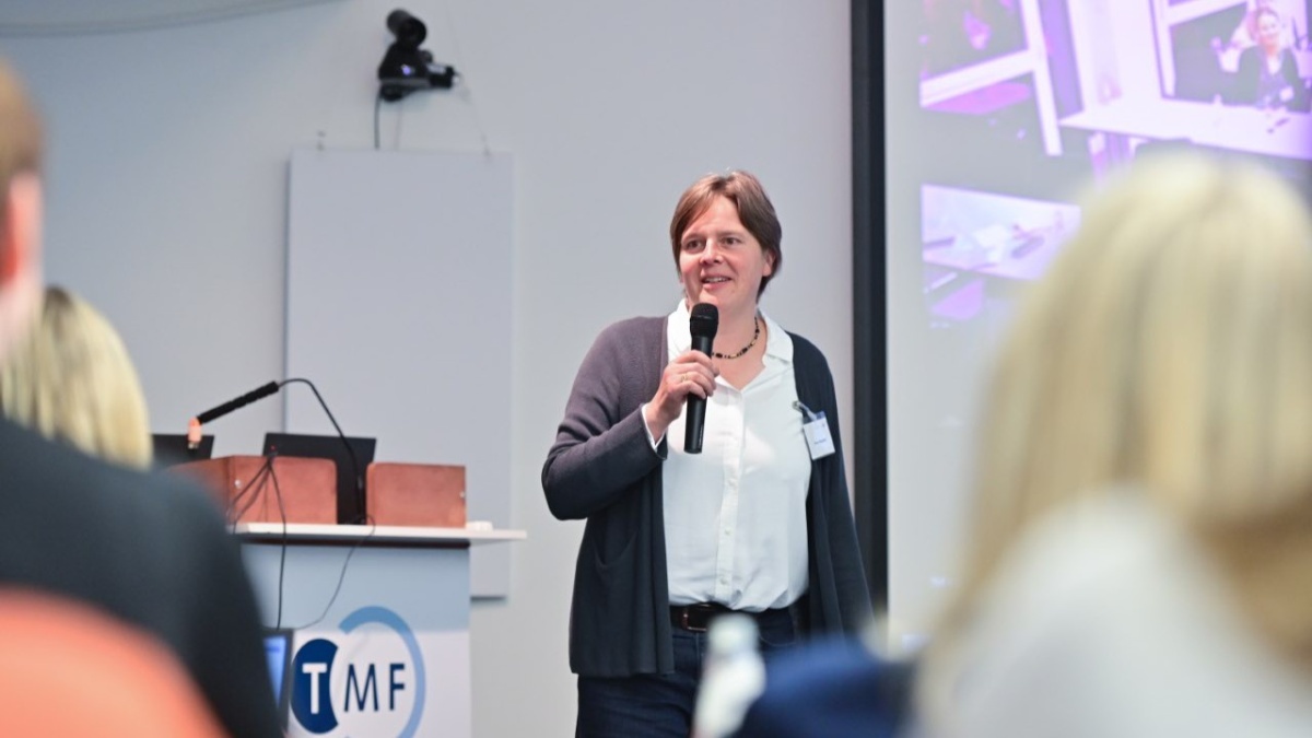 PD Dr. Anne C. Regierer spricht während des Kick-offs in ein Handmikrofon. Im Vordergrund sind mehrere Zuhörende unscharf zu sehen. Das TMF-Logo am Rednerpult ist auf der linken Seite sichtbar.