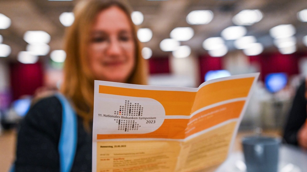Biobanken-Symposium 2023 Eine Frau, die den Programmflyer des Biobanken-Symposiums 2023 in die Kamera hält