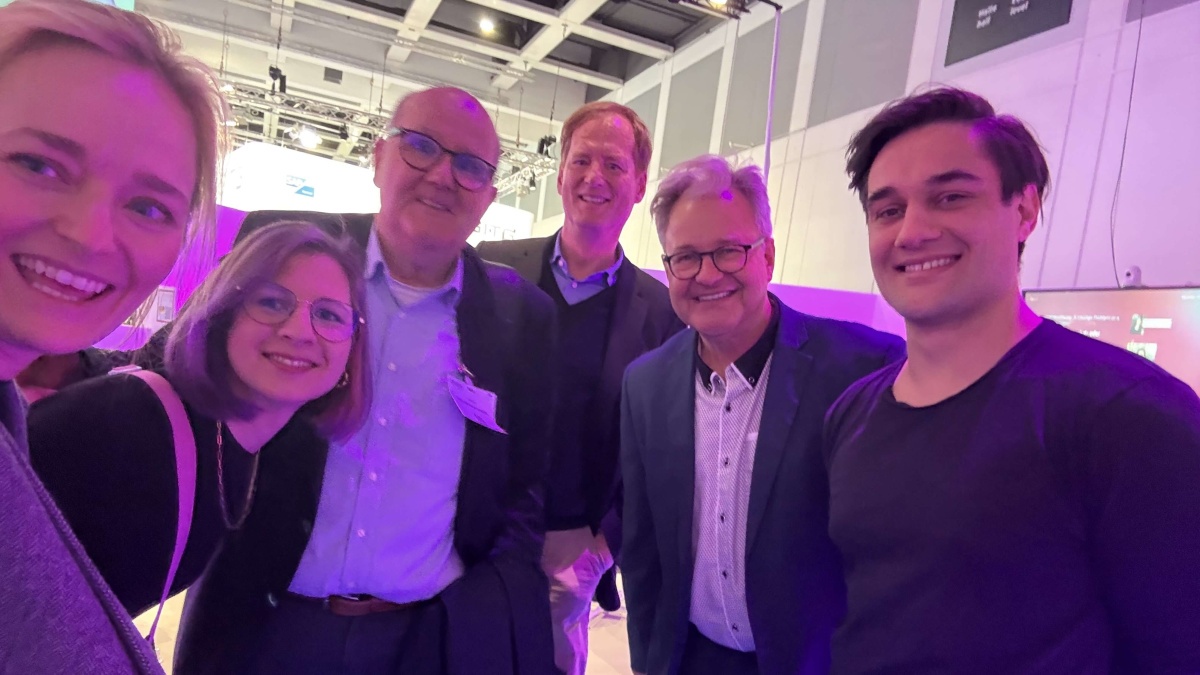 Sechs Personen lächeln für ein Gruppenselfie in eine Kamera.