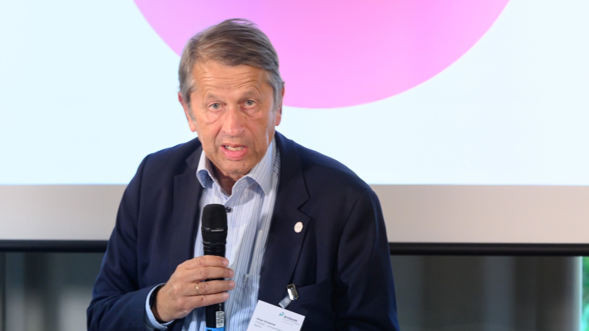 Ein Mann mit Anzug und Mikrofon steht vor einem Publikum.