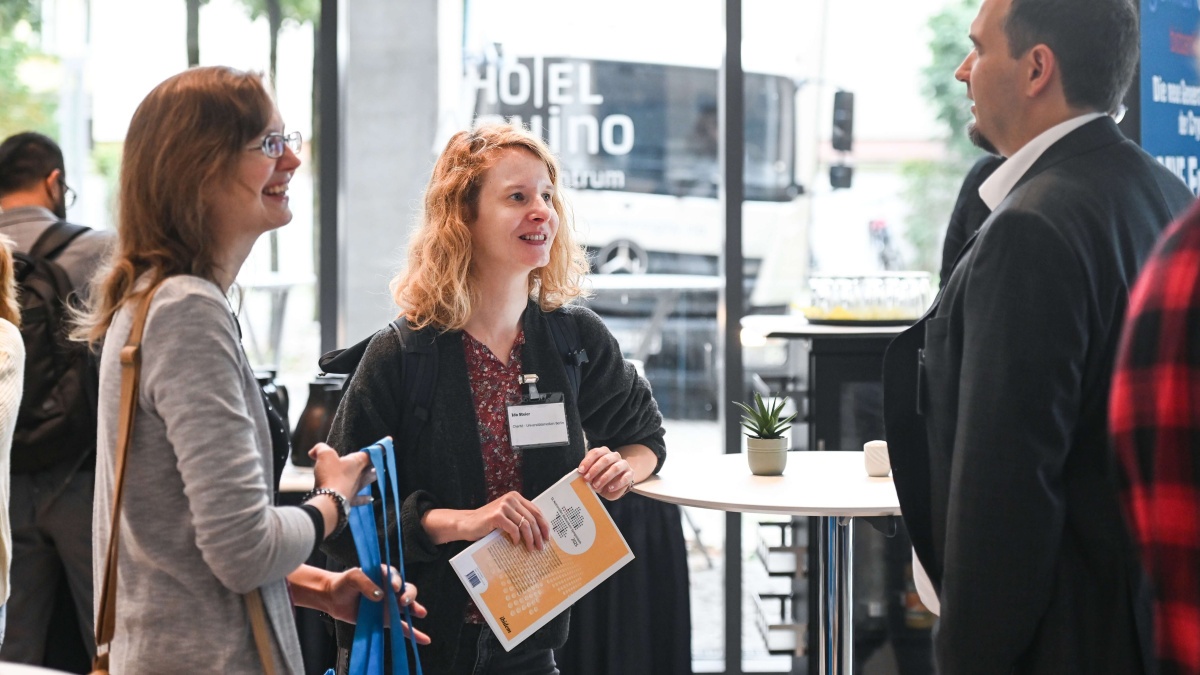 Biobanken-Symposium 2025 Drei Teilnehmende des Biobanken-Symposiums, die sich während einer Pause unterhalten. Eine Frau hält den Biobanken-Tagungsband.