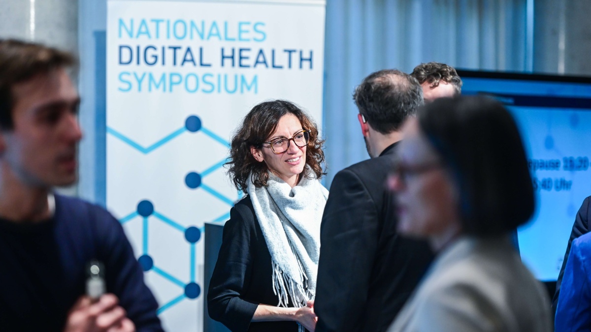 Mehrere Teilnehmende tauschen sich während einer Netzwerkpause aus. Im Hintergrund ist ein Roll-up mit der Aufschrift „Nationales Digital Health Symposium“ zu sehen.