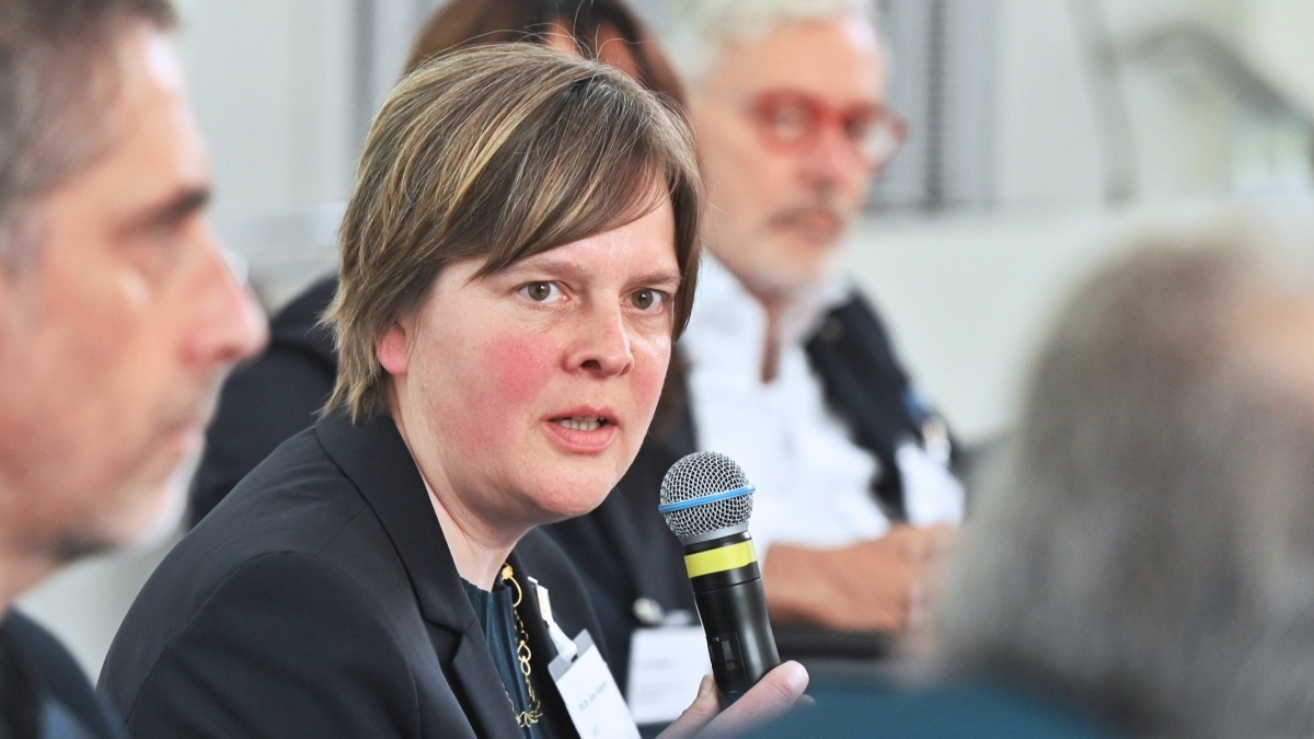 Eine Frau spricht in ein Mikrofon. Neben ihr sitzen weitere Teilnehmende der Paneldiskussion und hören zu.