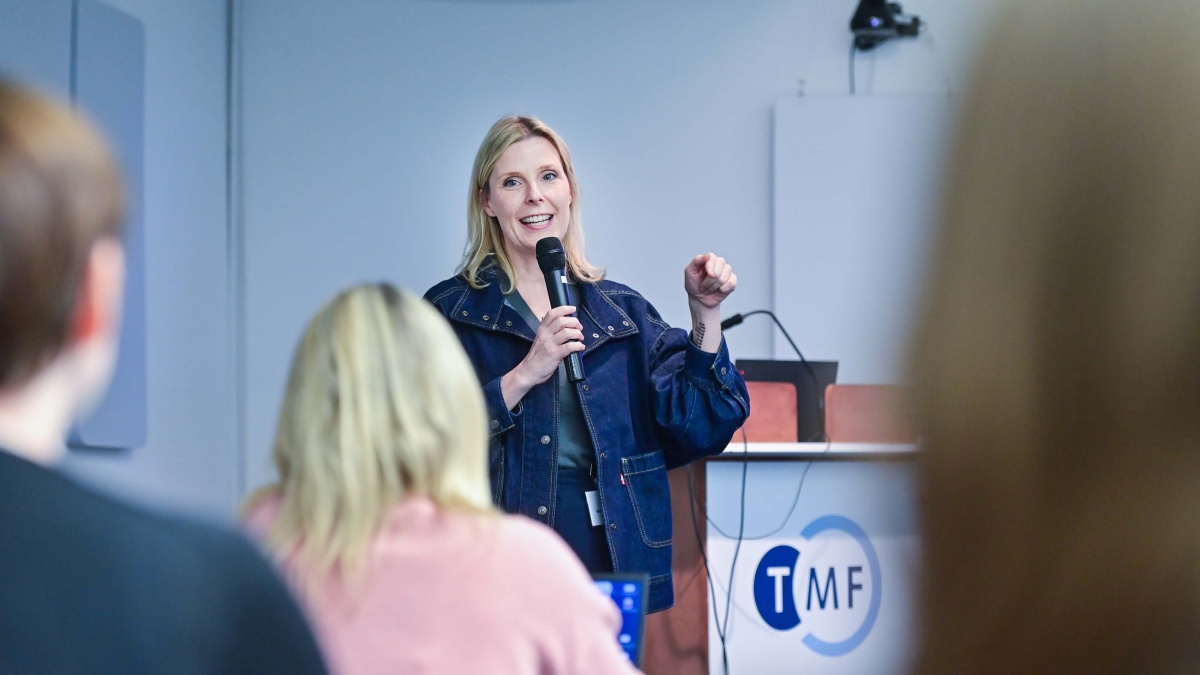 Prof. Dr. Sarah Hoffmann spricht beim Kick-off in ein Handmikrofon. Im Vordergrund sind unscharf Zuhörende zu sehen.
