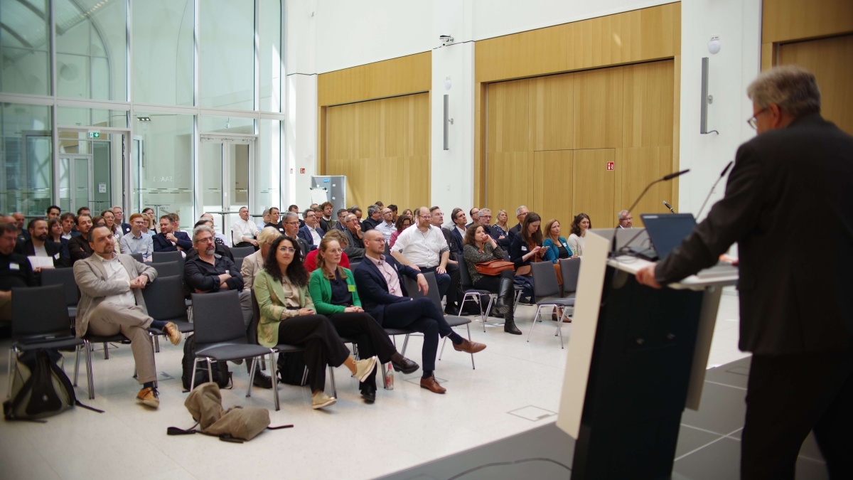 EHDS-Workshop Ein großer, teils vergläserter Raum, in dem links ein größeres Publikum und rechts ein Mann hinter einem Rednerpult zu sehen sind
