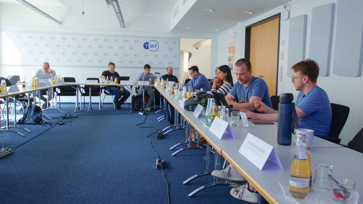 An mehreren Tischen, die in einer U-Form angeordnet sind, sitzen die Teilnehmenden Workshops.