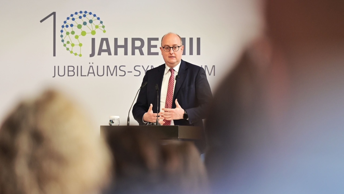 Ein Mann im Anzug und mit roter Krawatte steht an einem Rednerpult; im Hintergrund ist ein Banner mit der Aufschrift „10 Jahre MII Jubiläums-Symposium“ zu sehen.