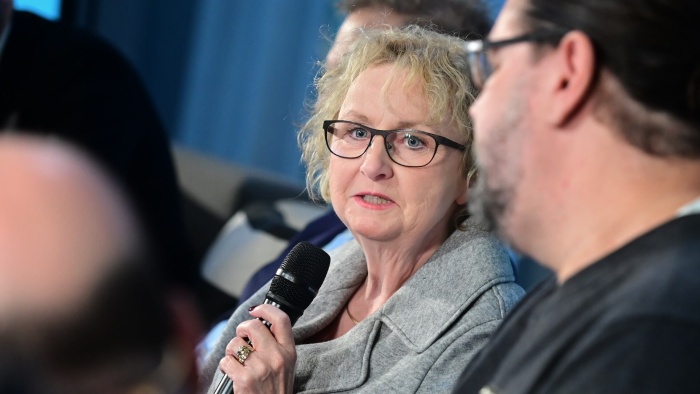 Dr. Christiane Wessel mit grauem Anzug und Brille. Sie spricht in ein Mikrofon.