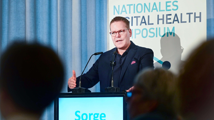 Tino Sorge, Parlamentarischer Staatssekretär im Bundesministerium für Gesundheit, steht an einem Podium und hält eine Ansprache vor Publikum; im Hintergrund ist der Schriftzug ‚Nationales Digital Health Symposium‘ zu sehen.